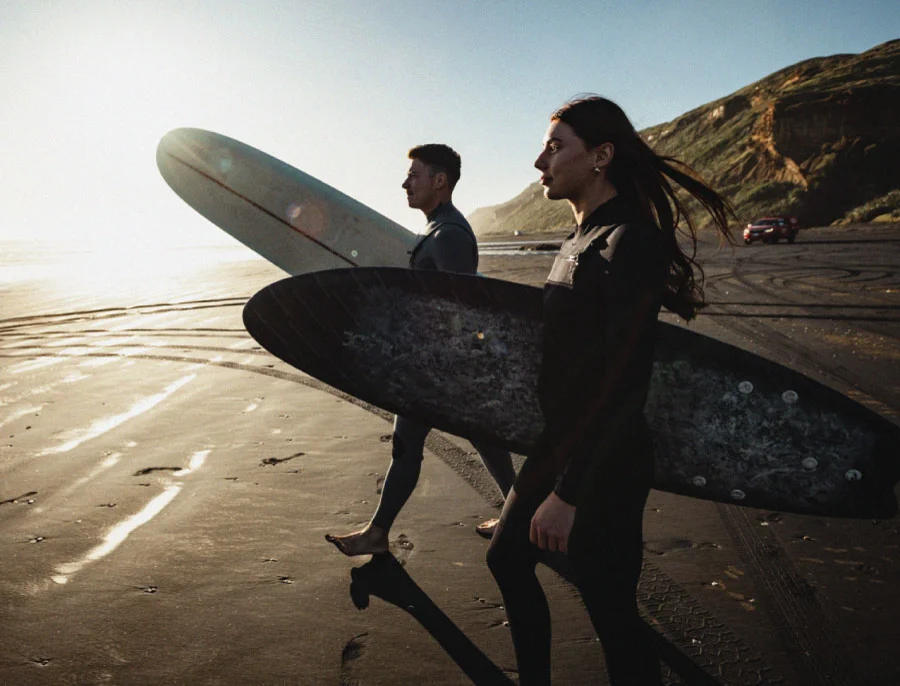 Two surfers walking together on a beach at sunset